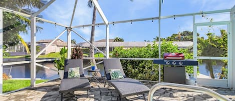 Un espacio al aire libre techado con sillones de descanso, una parrilla y vistas a un cuerpo de agua.