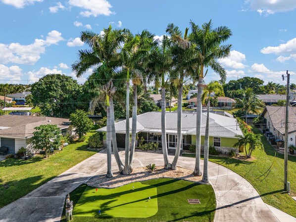 A residential area with a house surrounded by palm trees, a well-maintained lawn, and a clear sky.
