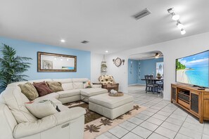 A living room with a sectional sofa, a dining area with a TV, and a ceiling fan.