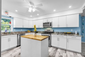 A modern kitchen with white cabinets, a central island, a microwave, and an oven.