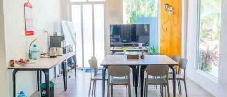 A dining area with a table and chairs, a television, and a window with a view of greenery.