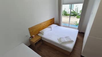 Een eenpersoonsbed met een houten hoofdbord in een kamer met een raam en uitzicht op groen.