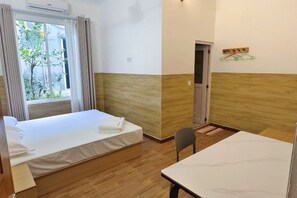 Une chambre d’hôtel avec un lit, une table et une chaise. Il y a une fenêtre avec des rideaux et une vue sur la verdure à l’extérieur.