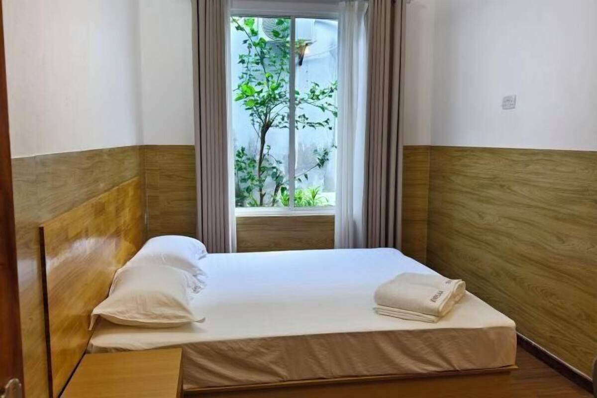 Un letto singolo con una testiera in legno, una finestra vista verde e una tenda.