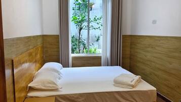 A single bed with a wooden headboard, a window with a view of greenery, and a curtain.