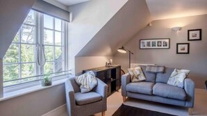 A modern living room with a sofa and armchair, a small side table, a lamp, and framed pictures on the wall. - 29 Rhodewood House - 2 Bedroom - Saundersfoot (Saundersfoot)