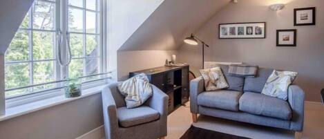 A modern living room with a sofa and armchair, a small side table, a lamp, and framed pictures on the wall.