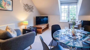 A modern living room with a flat-screen TV, a dining table set for four, and a cozy seating area. - 29 Rhodewood House - 2 Bedroom - Saundersfoot (Saundersfoot)