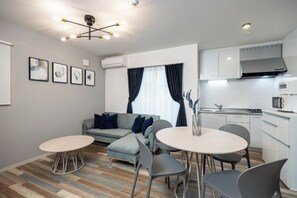 A modern living room with a sofa, dining table, and chairs, a kitchenette, and artwork on the wall. - WARAKU (Osaka)