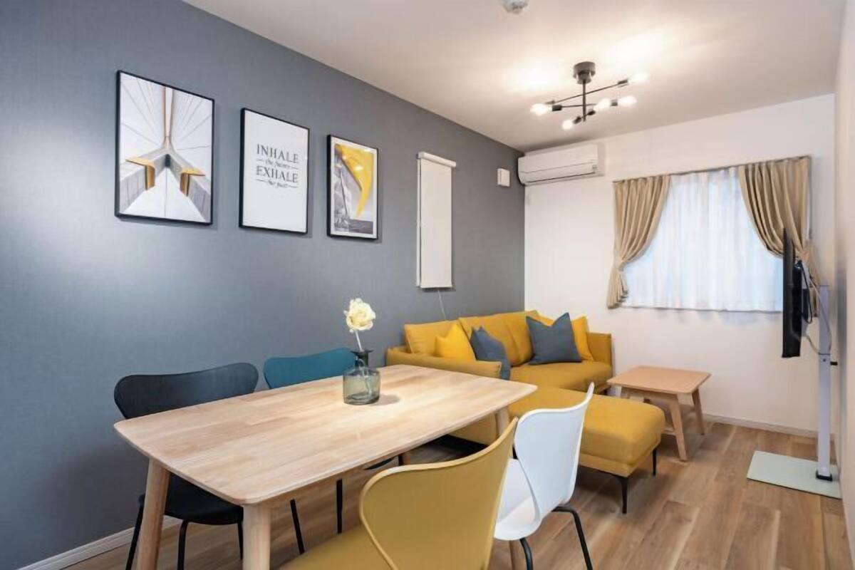 Una habitación moderna con una mesa de comedor, sillas, un sofá y una mesita. Hay cuadros en la pared y un equipo de aire acondicionado.