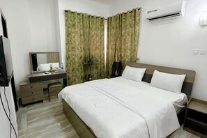 A bedroom with a bed, a desk, a mirror, and a wardrobe.