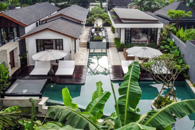 A modern villa with a central swimming pool, surrounded by lush greenery and outdoor seating areas.