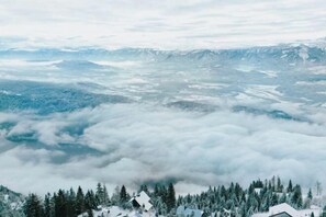 A panoramic view of a mountainous area with snow-covered houses and dense forests. - Luxescape-No 2306-Traumaussicht-Ski & Wandergebiet-Paragleiten-Langlauf-Parkplatz (Treffen bei Villach)