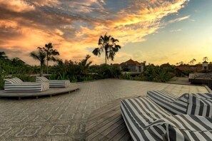 A rooftop lounge area with lounge chairs, palm trees, and a sunset view. - vila deh simba at seminyak aramanis (Bali)