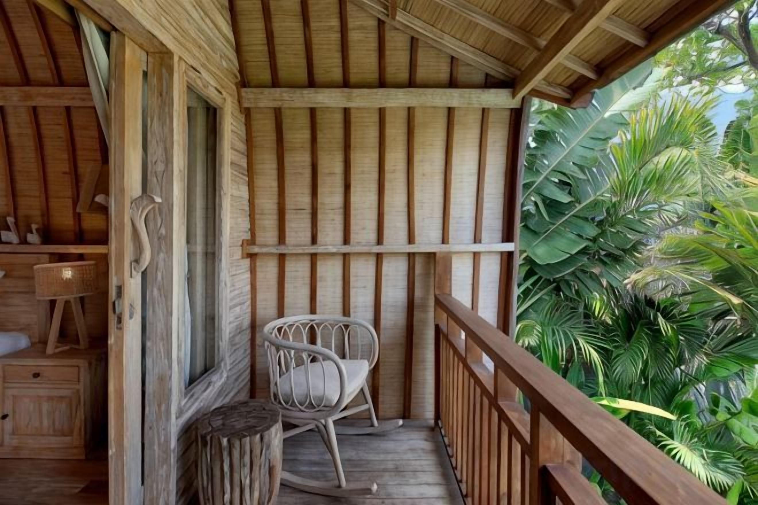A wooden balcony with a wooden railing, a wicker chair, and a small table.