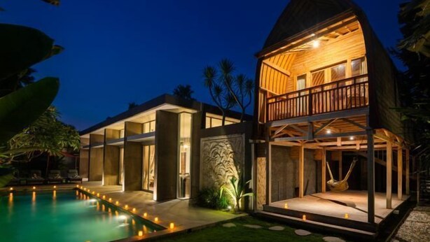 Ein Resort mit zwei Stockwerken, einem Schwimmbad, einer Hängematte und einer gut beleuchteten Außenfassade.