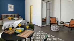 A modern hotel room with a bed, a dining table with chairs, a sofa, and a small round table with a bowl and glasses. - The Printhouse Downtown Studio 10 (Haifa)