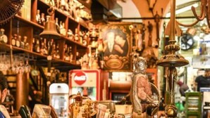 A cluttered antique shop with various items on display, including a bell, a statue, and a Coca-Cola refrigerator. - The Printhouse Downtown Studio 10 (Haifa)