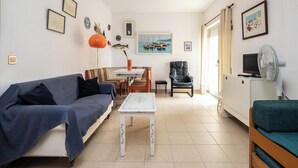 Ein Wohnzimmer mit einer Couch, einem Tisch, einem Sessel, einem Fernseher und einem Ventilator.