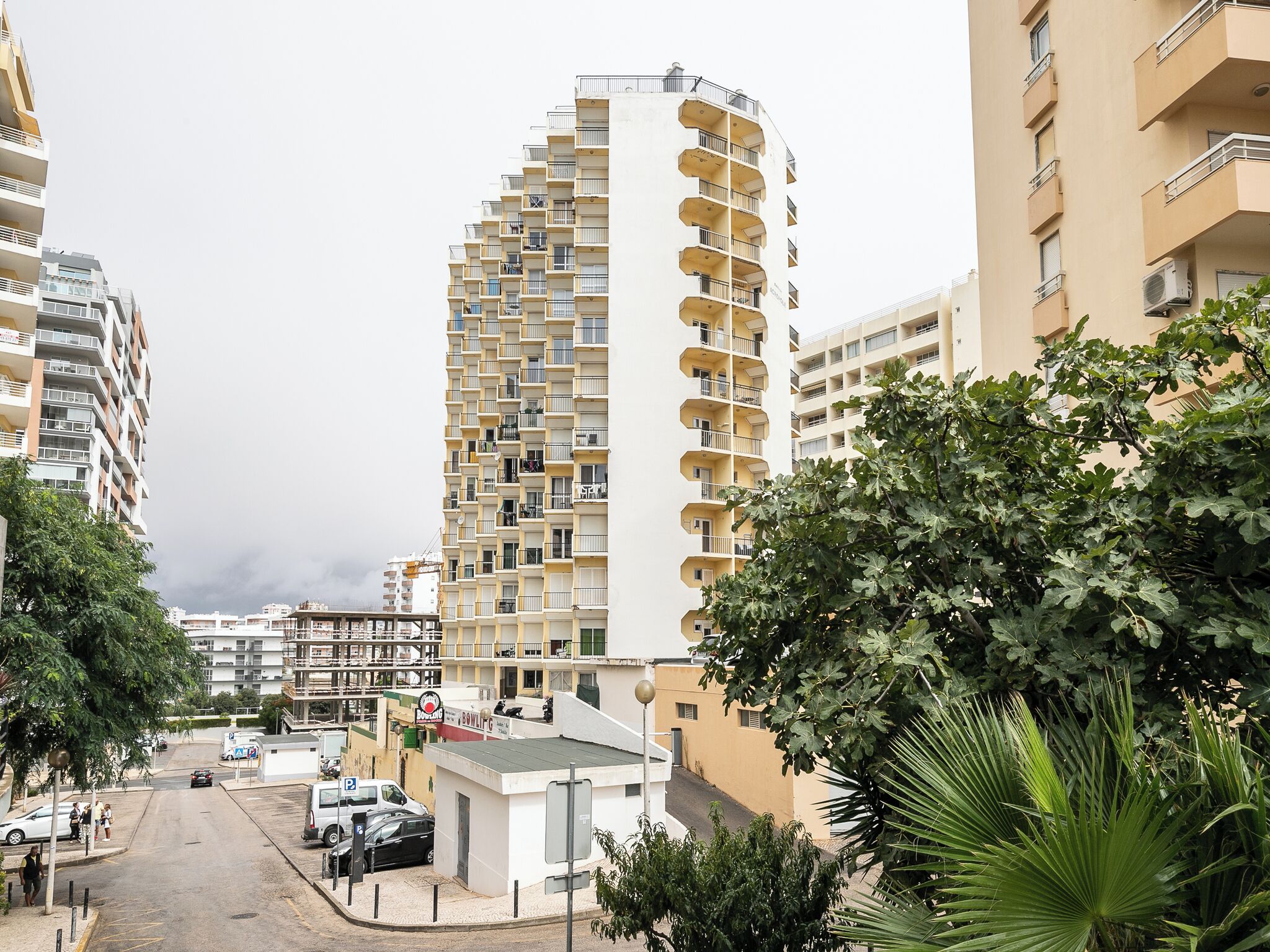 A multi-story residential building with balconies, a parking area, and surrounding greenery.