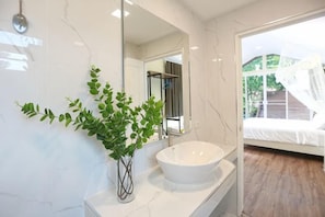 A bathroom with a white marble sink, a large mirror, and a potted plant.