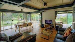 A spacious living room with a large TV, comfortable seating, and a dining area with a view of the garden. - Little Tree House(3 bedrooms) (Pak Chong)