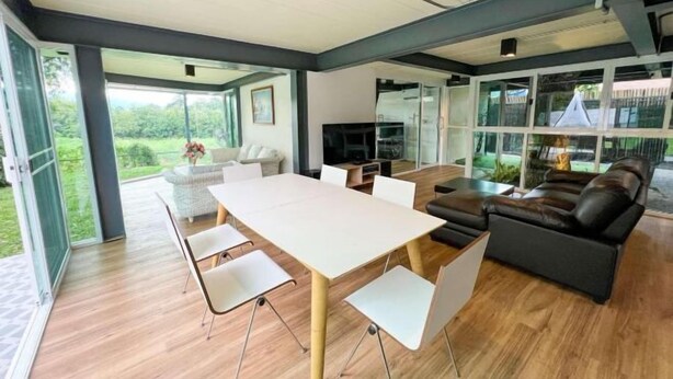 A modern living room with a large table, comfortable seating, and large windows offering a view of the outdoors. - Little Tree House(3 bedrooms) (Pak Chong)