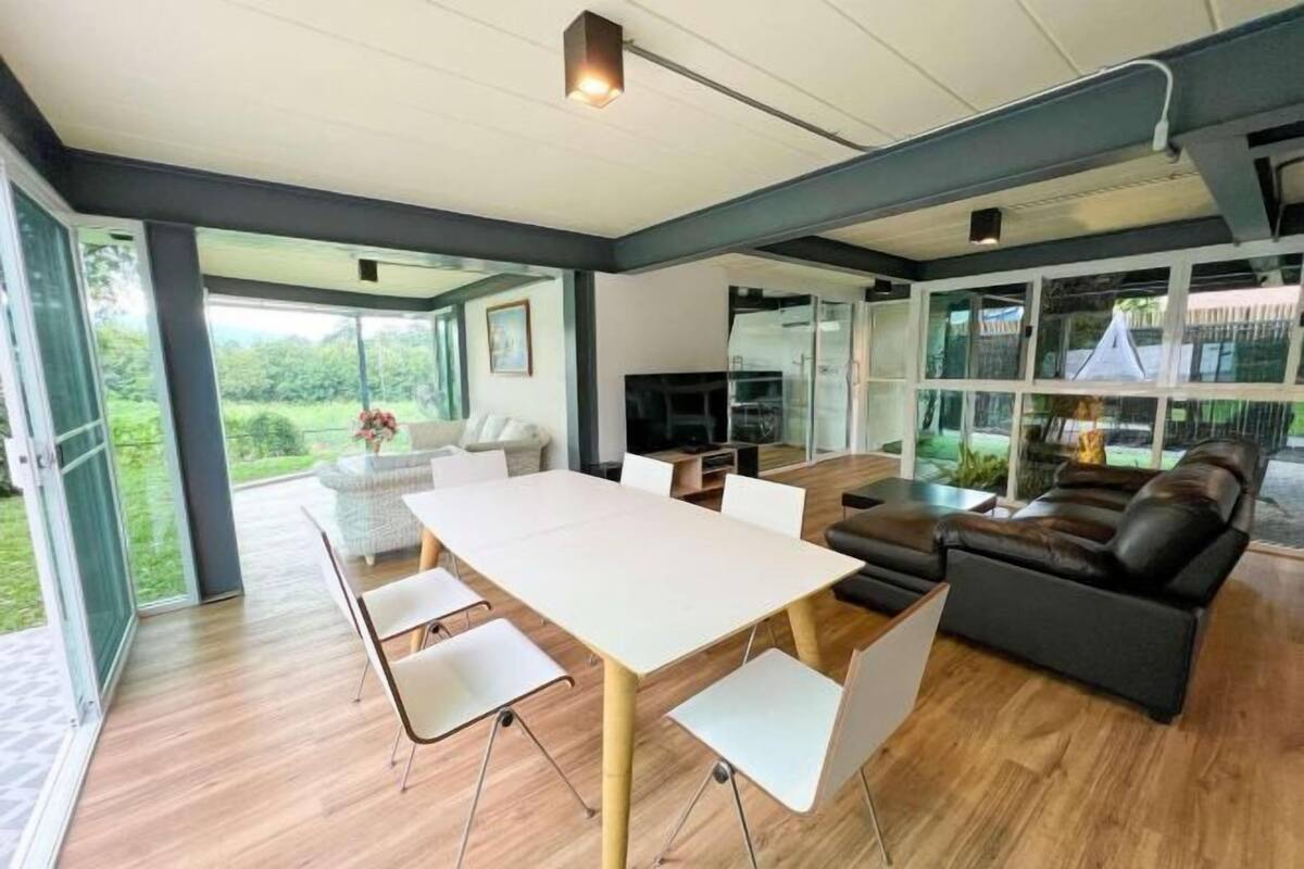 A modern living room with a large table, comfortable seating, and large windows offering a view of the outdoors.