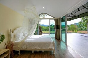 A bedroom with a bed, a bedside table, a window, and a view of the outdoors.