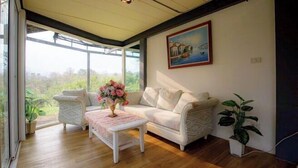 A room with a sofa, a coffee table with flowers, a potted plant, and a painting on the wall. - Little Tree House(3 bedrooms) (Pak Chong)