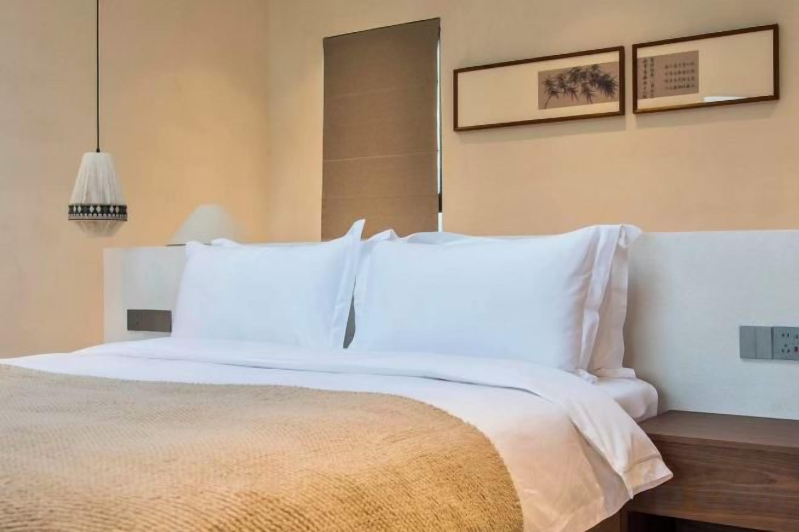 A hotel room with a bed, bedside table, lamp, and wall-mounted artwork.