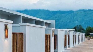 A row of white hotel rooms with wooden doors and a view of mountains.