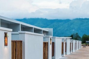 A row of white hotel rooms with wooden doors and a view of mountains.