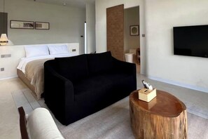A modern hotel room with a bed, a black sofa, a round wooden coffee table, and a TV mounted on the wall. - Resort By Allpoints (Anouvong)