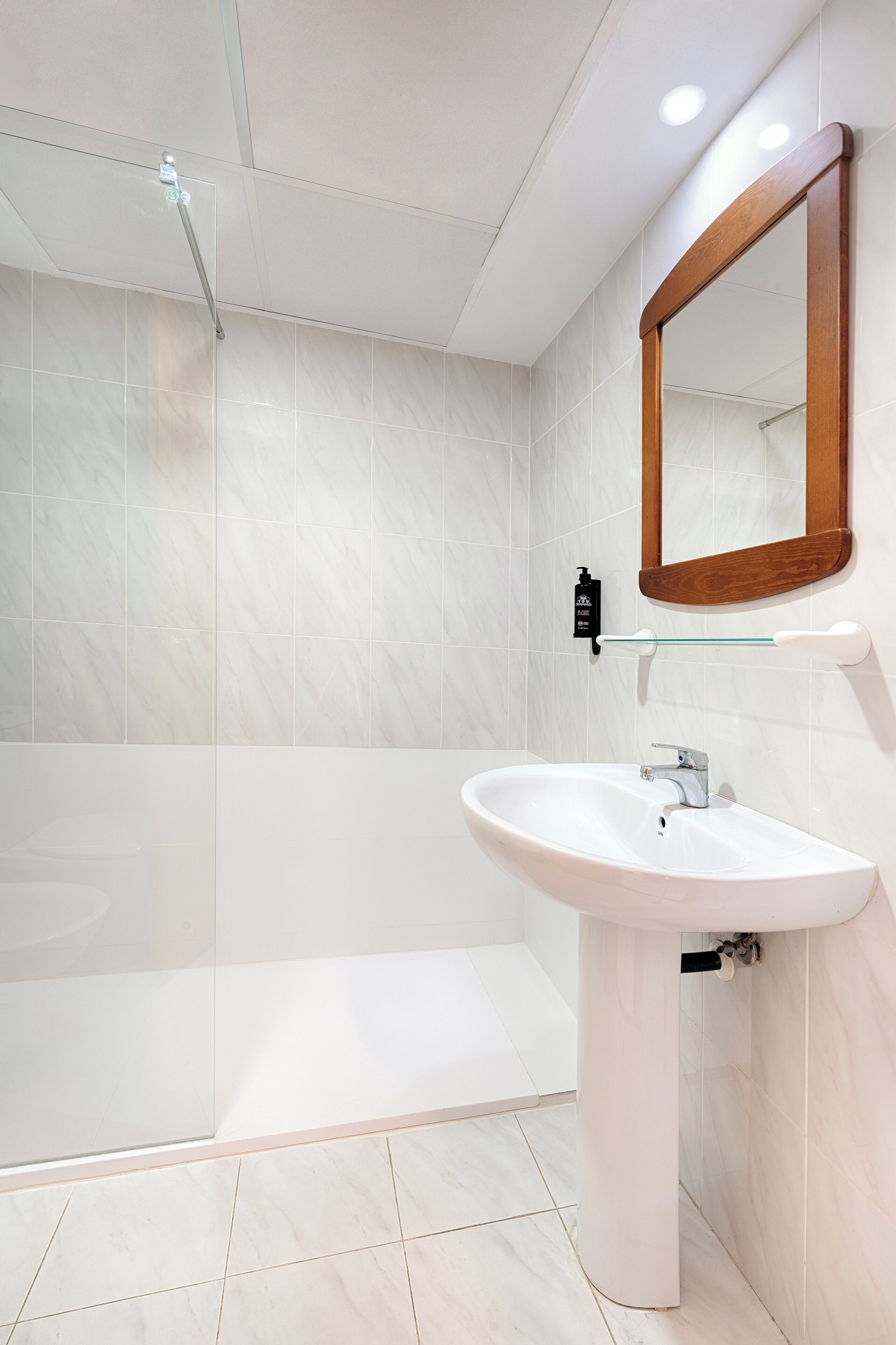 A bathroom with a white sink, a glass shower enclosure, and a wooden-framed mirror.