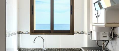 A kitchen with a stainless steel sink, a window with a view of the sea, and a coffee machine.