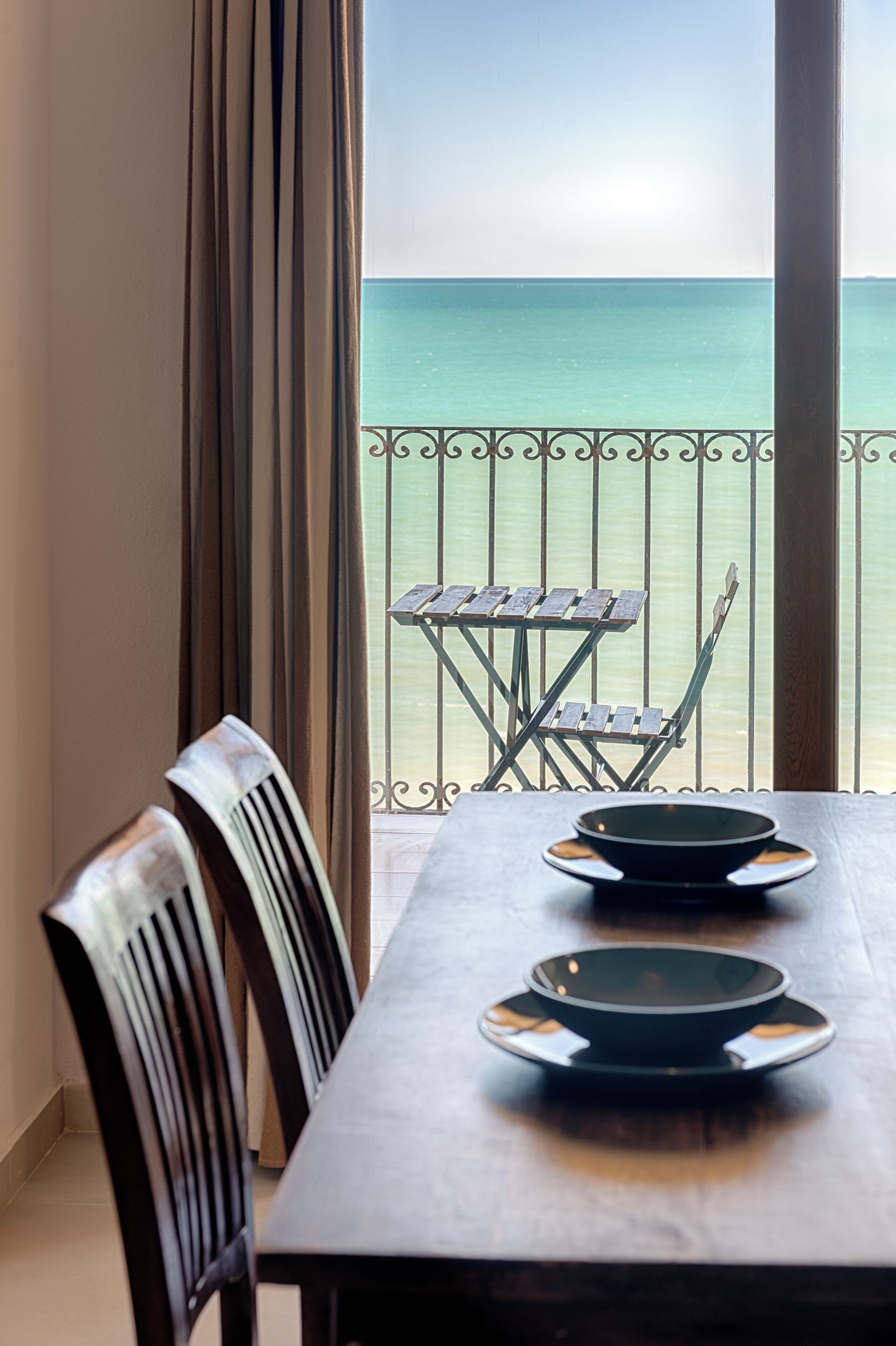 A dining table with chairs and a view of the sea through a balcony railing.