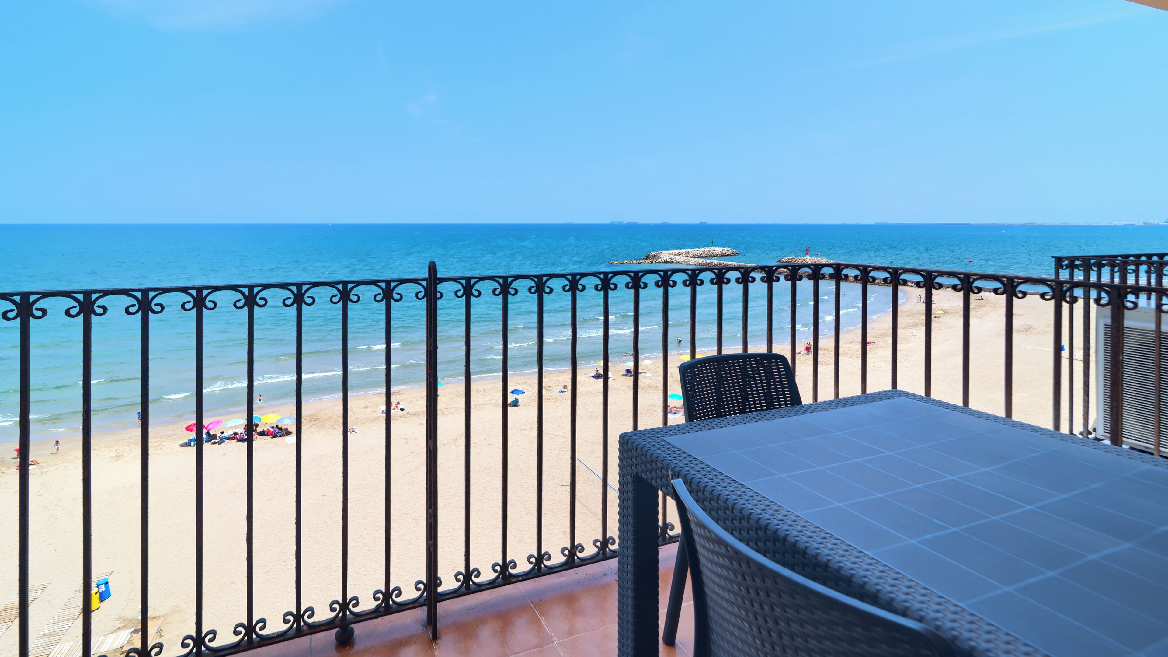 A balcony with a view of the beach, a table, and a chair.