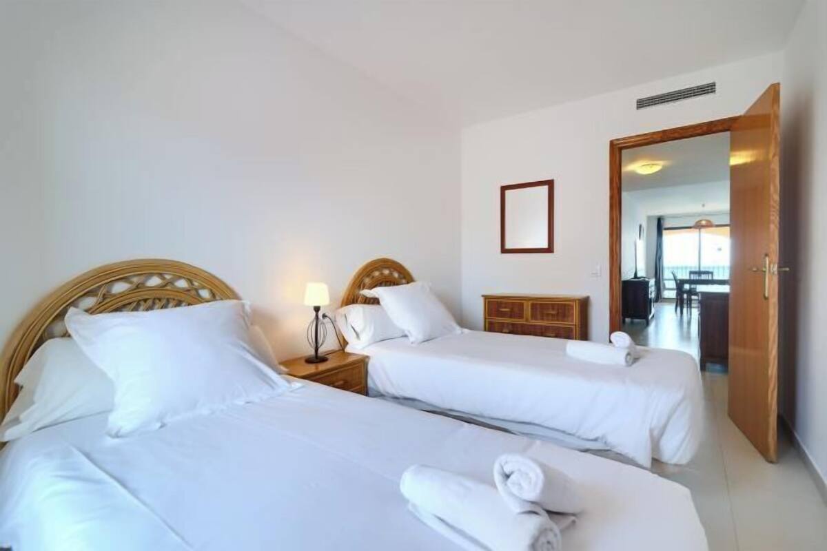 Habitació d'hotel amb dos llits, un panell de capçalera de fusta, una taula de nit amb una làmpada, un taulell de fusta i un mirall a la paret.