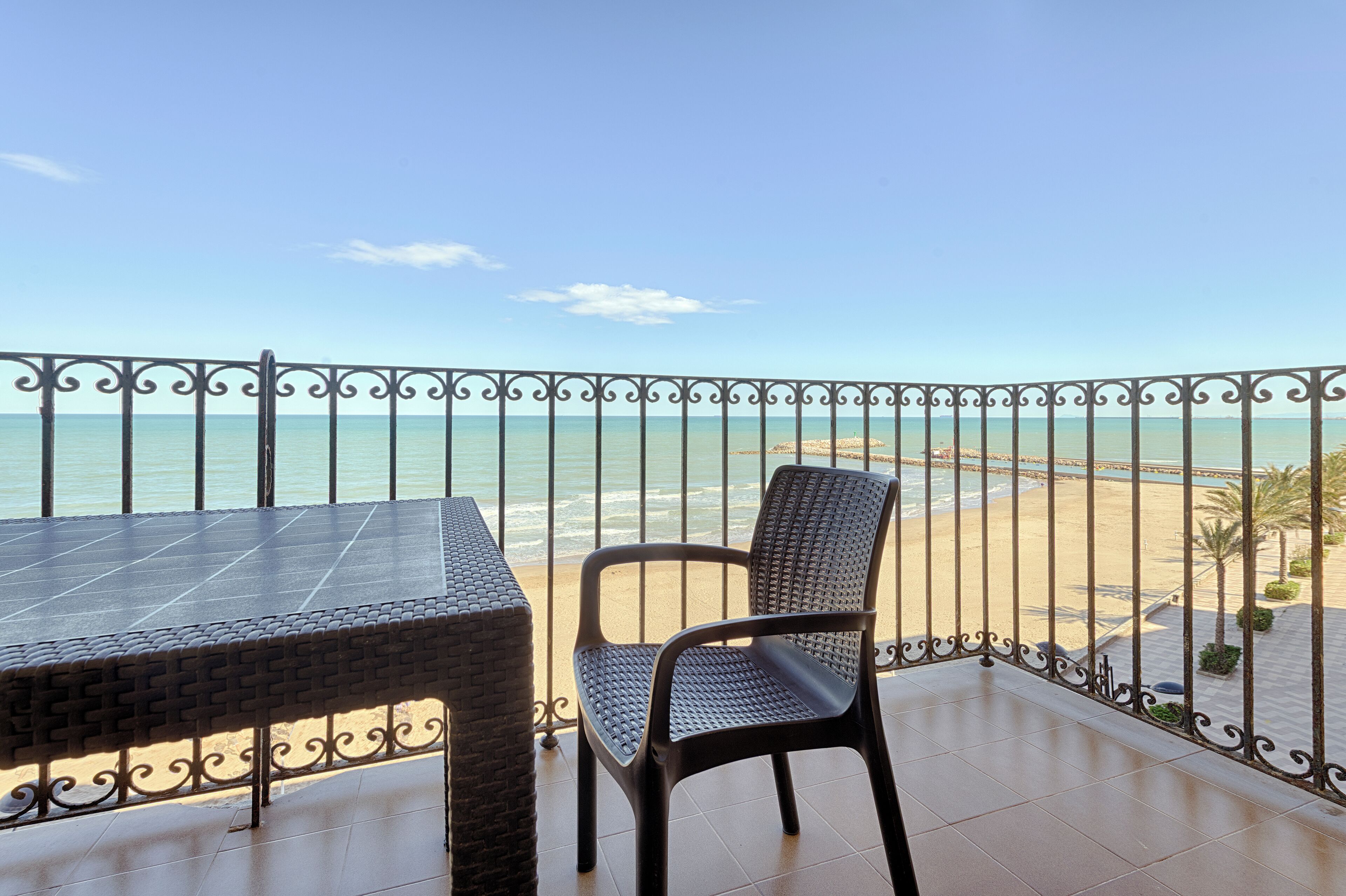 Un balcón con vista a la playa, una mesa y una silla.