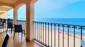 Un balcón con vista a la playa, una silla y una mesa.