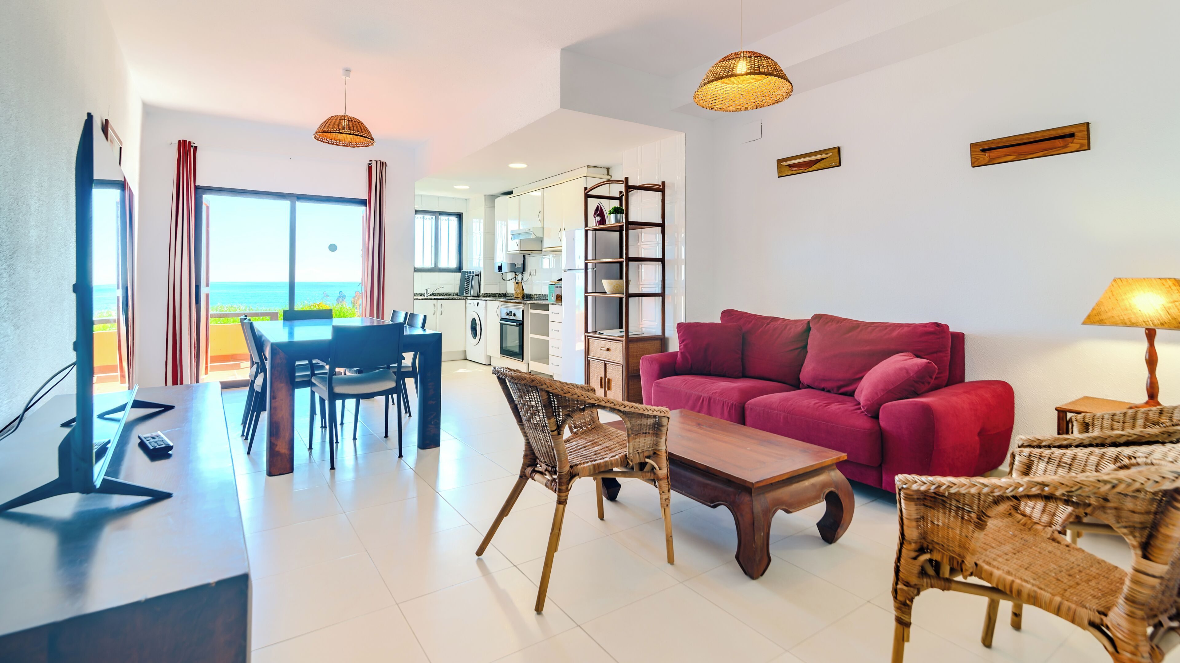 A modern living room with a red sofa, wicker chairs, a wooden coffee table, and a dining area with a table and chairs.