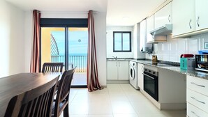 Una cocina moderna con armarios blancos, horno empotrado y comedor con mesa y sillas de madera.