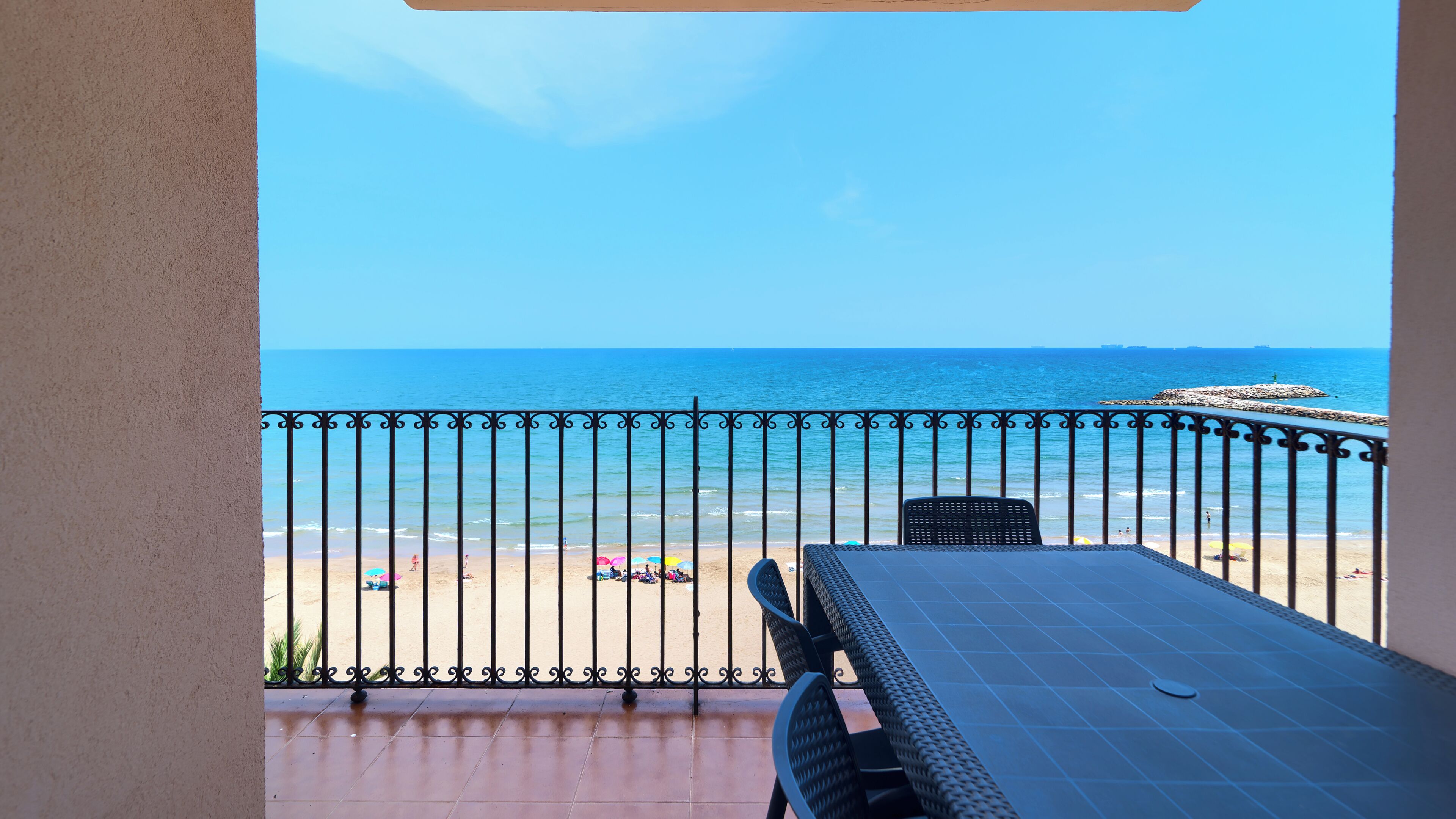 A balcony with a view of the sea, a tiled floor, and a metal railing.