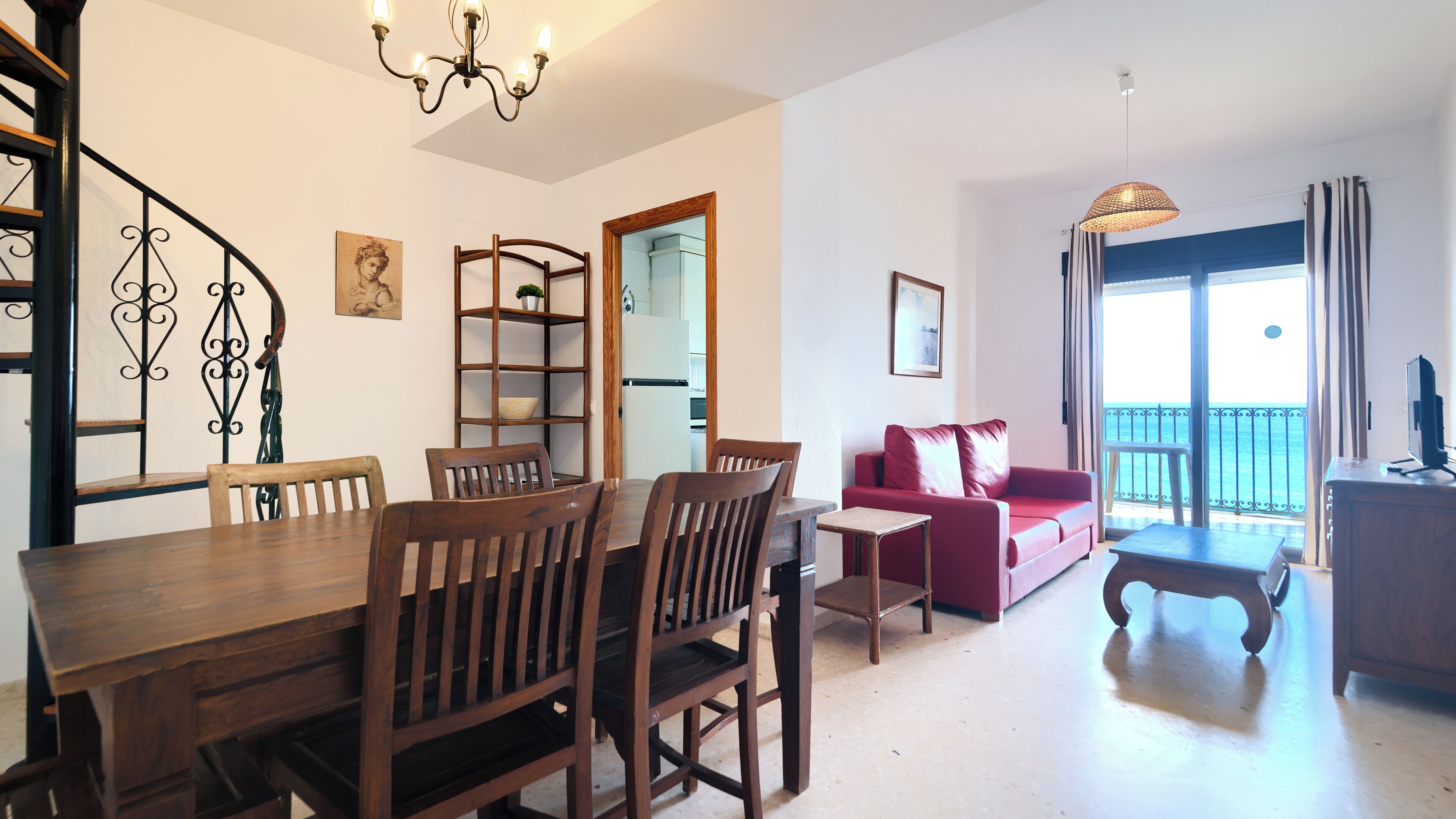 A dining area with a wooden table and chairs, a red sofa, a TV, and a balcony with a view.