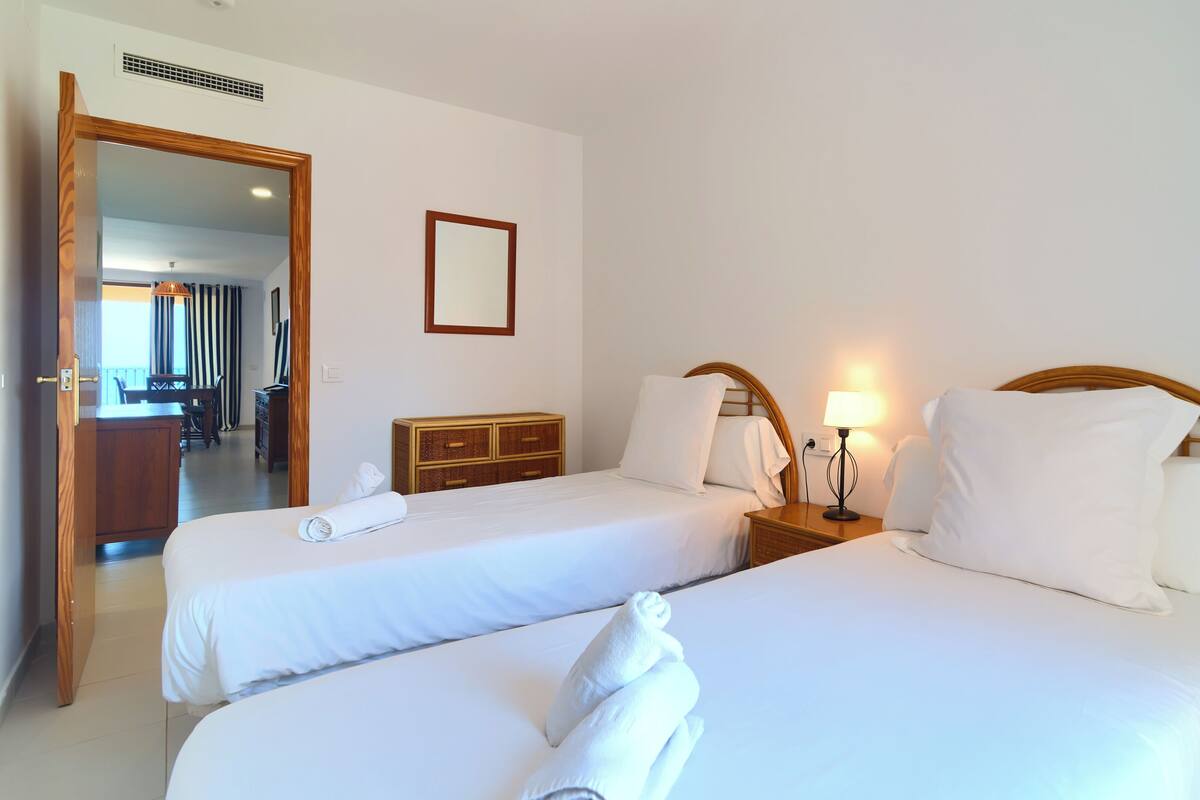 Habitació d'hotel amb dos llits, un taulell de nit de fusta, un mirall i un escriptori amb cadires.