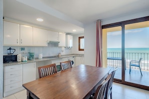 A kitchen with white cabinets, a wooden dining table, and a view of the ocean through a sliding glass door. - Sea You Aptos Valencia Port Saplaya  (Port Saplaya)