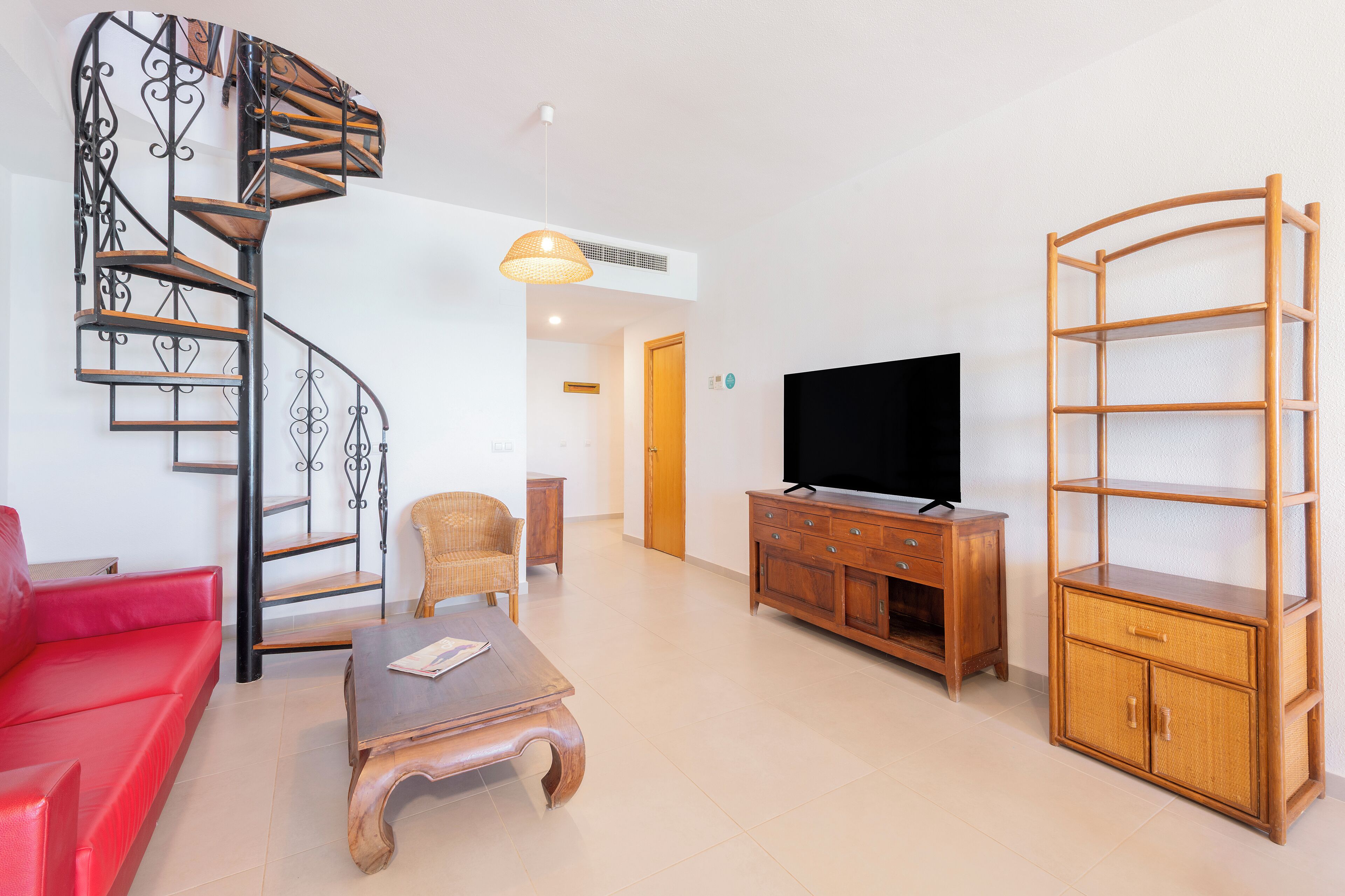 Un salon avec un escalier en colimaçon, un canapé rouge, une table basse en bois, un téléviseur et un meuble en bois.