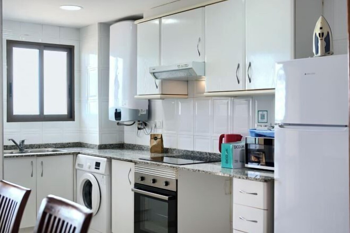 Une cuisine compacte avec des meubles blancs, un four encastré, un lave-linge et un four à micro-ondes.