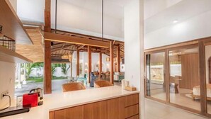 A modern kitchen with wooden cabinets, a white countertop, and a view of the outdoor area. - Villa Elora Canggu (Bali)